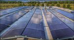 Een close-up van het dak van het Eemhuis bedekt met zonnepanelen, met op de achtergrond bomen en een blauwe lucht.