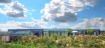 Het Eemhuis. Een modern gebouw met grote ramen, omringd door een bloeiende tuin en onder een heldere blauwe lucht met wolken.