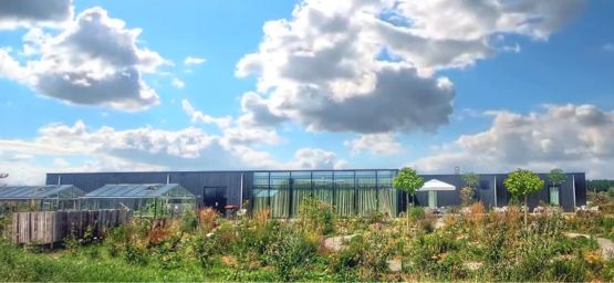 Het Eemhuis. Een modern gebouw met grote ramen, omringd door een bloeiende tuin en onder een heldere blauwe lucht met wolken.