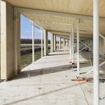 Een deels afgewerkt longhouse, met houten plafonds en metalen steunpilaren. De vloer is van beton en er zijn verschillende bouwmaterialen en gereedschappen zichtbaar.